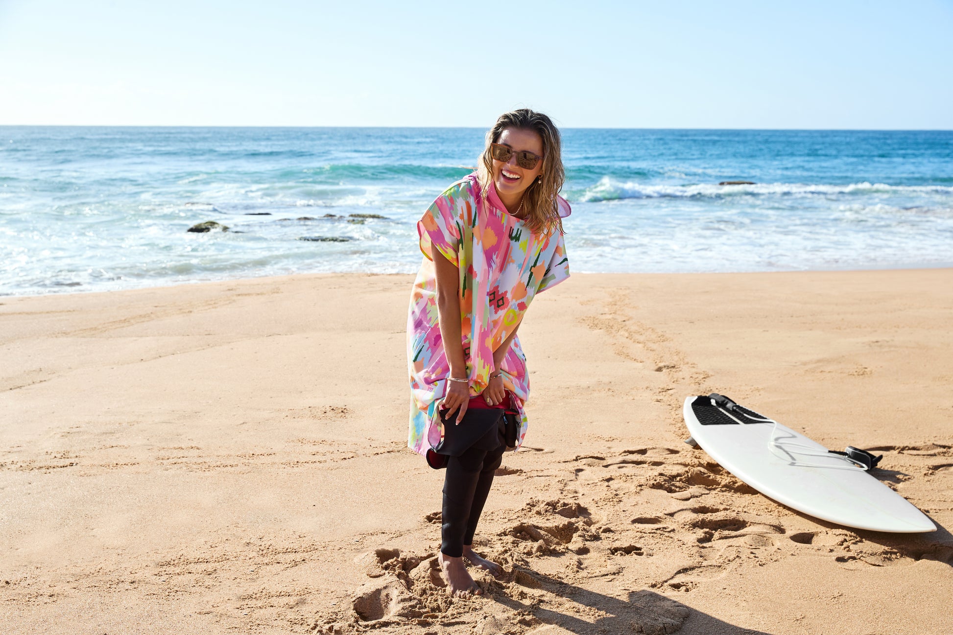 Woman in a colorful shirt standing on a beach with a surfboard nearby